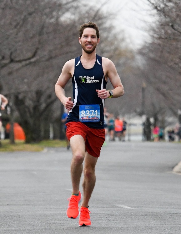John Stilling running on a paved roadway in a navy blue DC Road Runners singlet