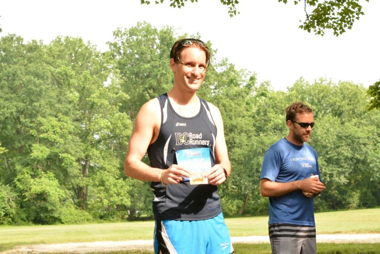 Joseph P Fisher wearing a navy blue DC Road Runners singlet holding an award gift card after a race