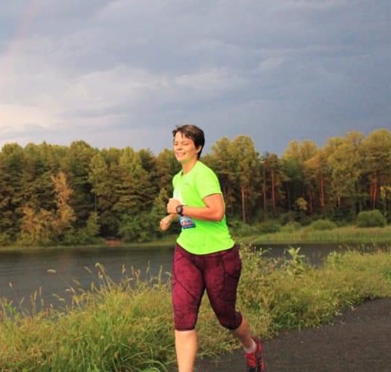 Roxann Dzur jogging by a lake on a grey day wearing a bright green shirt and red jogging pants